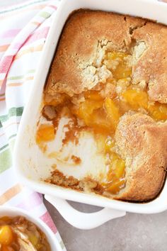 a casserole dish filled with peach cobbler next to a bowl of fruit