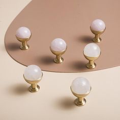 several white and gold knobs on top of a pink table with an oval mirror in the background