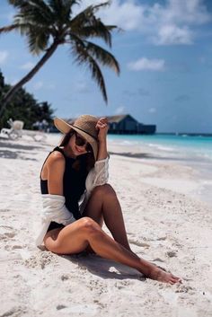 a woman is sitting on the beach with her legs crossed and wearing a straw hat