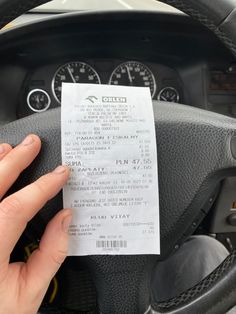 a hand holding a ticket in front of a car steering wheel