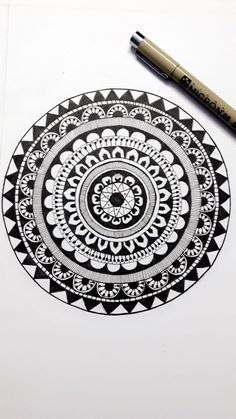 a black and white drawing of a circular design on paper with a marker next to it