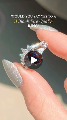 a woman's hand holding a ring with a black fire opal in it