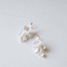 two small white flowers are hanging from the back of ear clips on a white surface