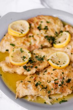 a white plate topped with chicken covered in lemon slices and sauce on top of a marble table