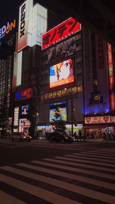 a city street at night with tall buildings and neon signs on the side of it