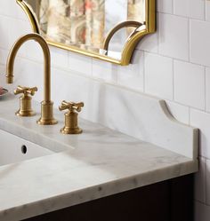 two golden faucets sit on a marble countertop in front of a mirror