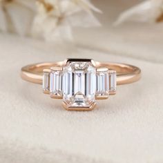 our Bezel Set Art Deco Unique Emerald Cut Moissanite Cluster Baguette Engagement Ring in 14K Rose Gold. This exquisite ring features a dazzling emerald-cut Moissanite stone surrounded by a cluster of sparkling baguette diamonds, all set in a beautiful rose gold band. Art Deco Rose Gold Diamond Ring, Art Deco Diamond Ring With Baguette Diamonds, Art Deco Emerald Cut Diamond Ring With Baguette Diamonds, Rose Gold Moissanite Diamond Ring In Baguette Cut, Rose Gold Moissanite Diamond Ring With Baguette Cut, Art Deco Baguette Cut Diamond Ring, Art Deco Diamond Ring With Square Cut For Wedding, Art Deco Square Cut Diamond Wedding Ring, Baguette Engagement Ring