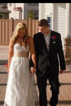 a young man and woman dressed in formal wear walking down the street together holding hands