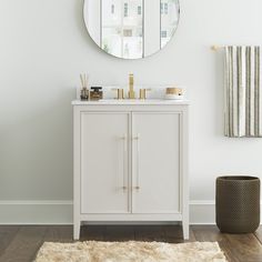 a white bathroom with a round mirror above the sink and rug on the floor next to it