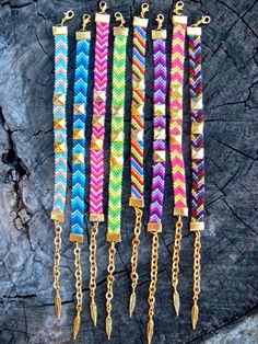 five different colored bracelets with gold chains on top of a piece of tree trunk