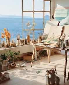 an artist's studio overlooking the ocean with lots of plants and vases on the table