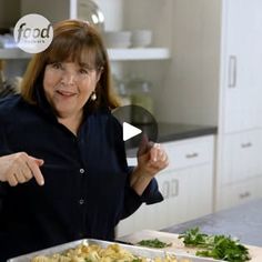 a woman standing in front of a pan with food on it and pointing to the side