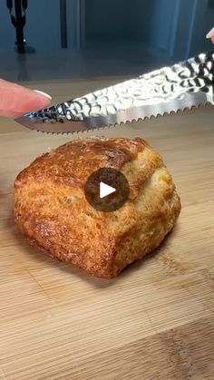 a person holding a knife over a piece of bread on top of a wooden table