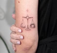 a woman with a tattoo on her arm holding a scale and sun in the background