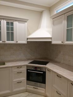 an empty kitchen with white cabinets and marble counter tops, along with a stainless steel range hood