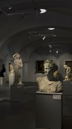 there are many statues on display in the room with white walls and ceiling lights above them