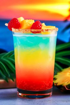 a colorful drink sitting on top of a table next to pineapples and watermelon