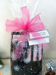 a christmas present in a black and white container with pink ribbon on it, next to some pine cones