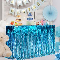 a teddy bear sitting in front of a table with blue streamers and cake on it