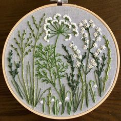 a close up of a embroidery on a wooden surface with white flowers and green leaves