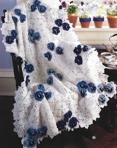 a white crocheted blanket with blue flowers on it in front of a window