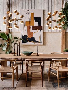 a dining room table surrounded by wooden chairs and art hanging on the wall behind it