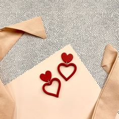 two red heart shaped earrings sitting on top of a piece of paper next to a ribbon