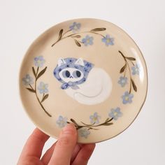 a hand holding a plate with a blue and white cat on it