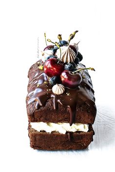 a piece of chocolate cake with cherries and whipped cream on top, sitting on a white surface