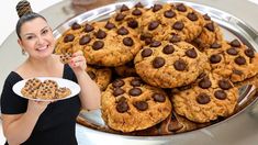 a woman holding a plate with cookies and chocolate chip cookies on it while standing in front of a platter