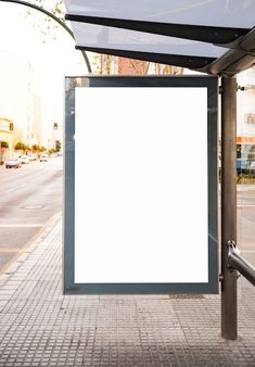 a bus stop with a white sign on the side of it's pole and buildings in the background