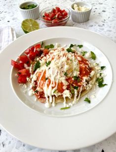 a white plate topped with food and garnished with toppings next to small bowls