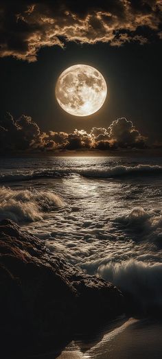 a full moon is seen over the ocean on a cloudy night with waves crashing in front of it