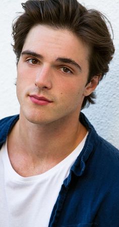 a close up of a person wearing a white shirt and blue cardigan jacket with his hair pulled back