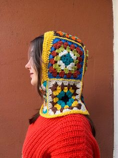 a woman wearing a crocheted hat with flowers on it's back, standing in front of a brown wall