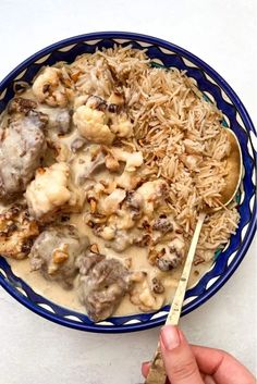 a blue bowl filled with rice and meat covered in gravy next to a spoon