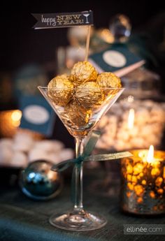 a martini glass filled with gold candies on top of a table next to candles