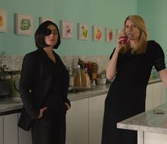 two women standing in a kitchen talking on the phone and looking at each other's eyes