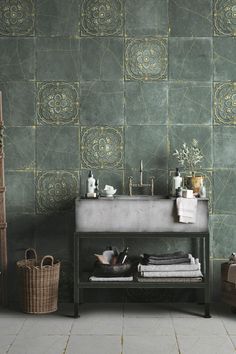 a bathroom with green tiled walls and flooring next to a wooden shelf filled with towels