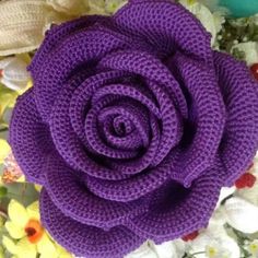 a knitted purple flower sitting on top of flowers