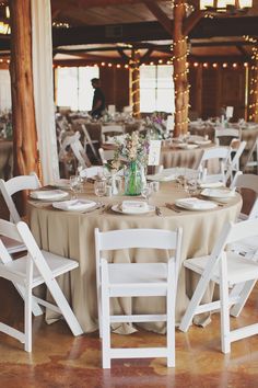 tables and chairs are set up for a wedding reception in the barn with lights strung from the ceiling