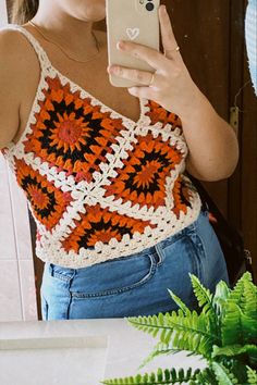 a woman is taking a selfie with her cell phone while wearing an orange and black crochet top