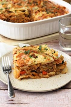 a white plate topped with lasagna next to a casserole dish filled with meat and vegetables