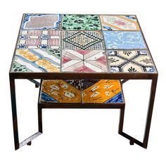 a multicolored table with metal legs and an open drawer on the top that has different designs on it