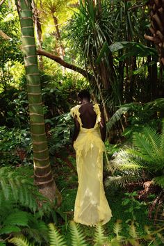 a woman in a yellow dress walking through the jungle