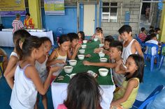 a group of young children sitting around a table eating and drinking from bowls on it