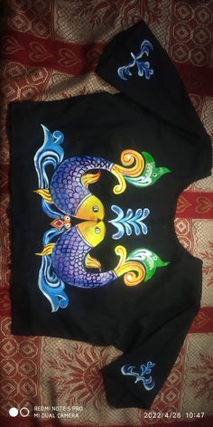 a black shirt with an image of a fish on the front and side, sitting on top of a bed