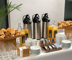 a table topped with plates and cups filled with breakfast foods next to bread, orange juice and croissants