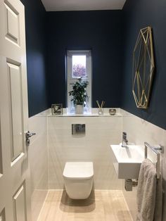 a white toilet sitting next to a sink in a bathroom under a window with blue walls