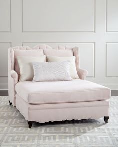 a pink chair with pillows on top of it in front of a white wall and carpet